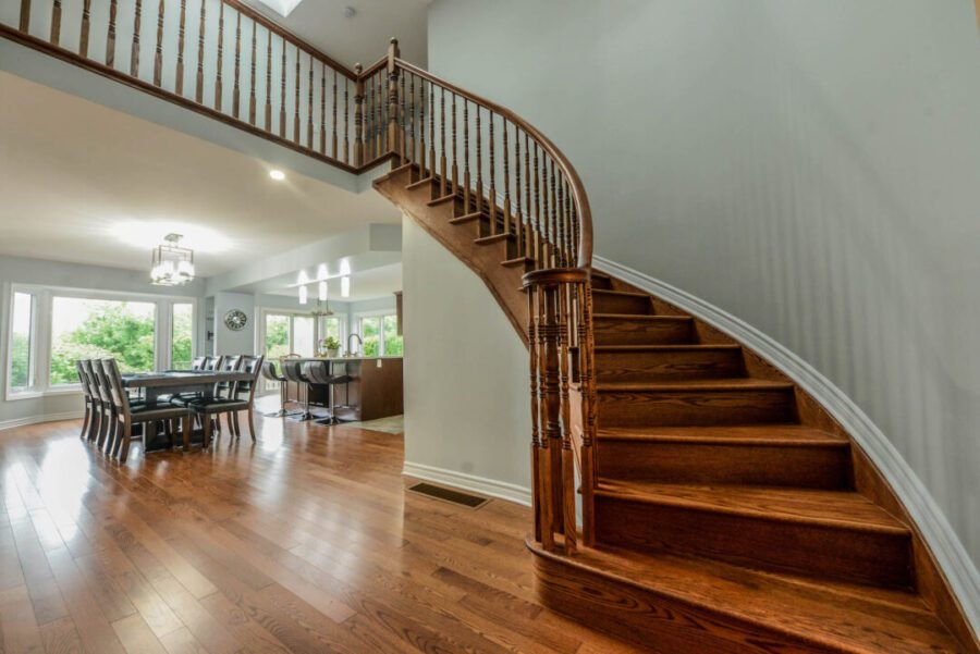 Main floor of an open concept home. Warm wood floors and light gray walls with a grand staircase curved to the right wall.