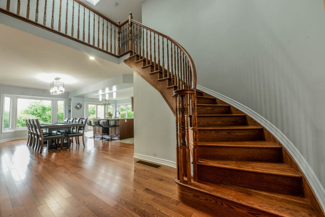 Main floor of an open concept home. Warm wood floors and light gray walls with a grand staircase curved to the right wall.