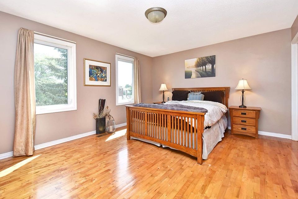 A family outside a row of townhouses in a suburban neighborhood. The townhouses are two stories and feature a combination of light-colored siding and stone accents on the facades, with gabled roofs. In the foreground, children are playing in the driveway, with a girl on a tricycle and a boy on a ride-on toy. A man and a woman are standing near the sidewalk talking, while another woman and child are entering one of the townhouses.