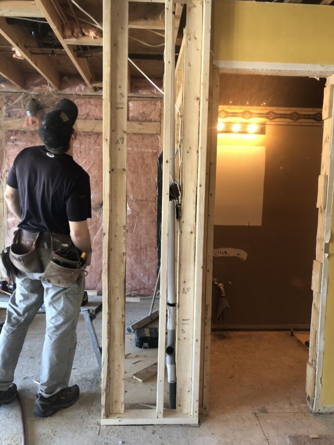 repair man looking up at an unfinished wall in a residential home.