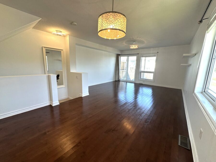 A large empty living room with clean wood floors, white walls and 3 ceiling lights.