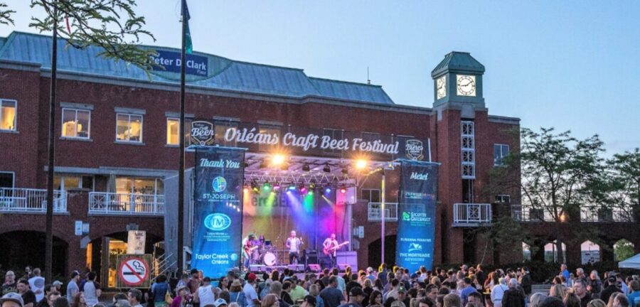 Image of a band playing on an outdoor stage with a big audience. Sign says "Orleans Craft beer Festival"